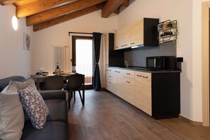 Un espace de vie compact comprenant un coin cuisine, un coin repas et un canapé agrémenté de coussins à motifs.