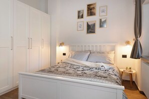 A bedroom with a bed, a wardrobe, a bedside table, and wall-mounted artwork. - Rosa Canina - three-room apartment with balcony (Roisan)