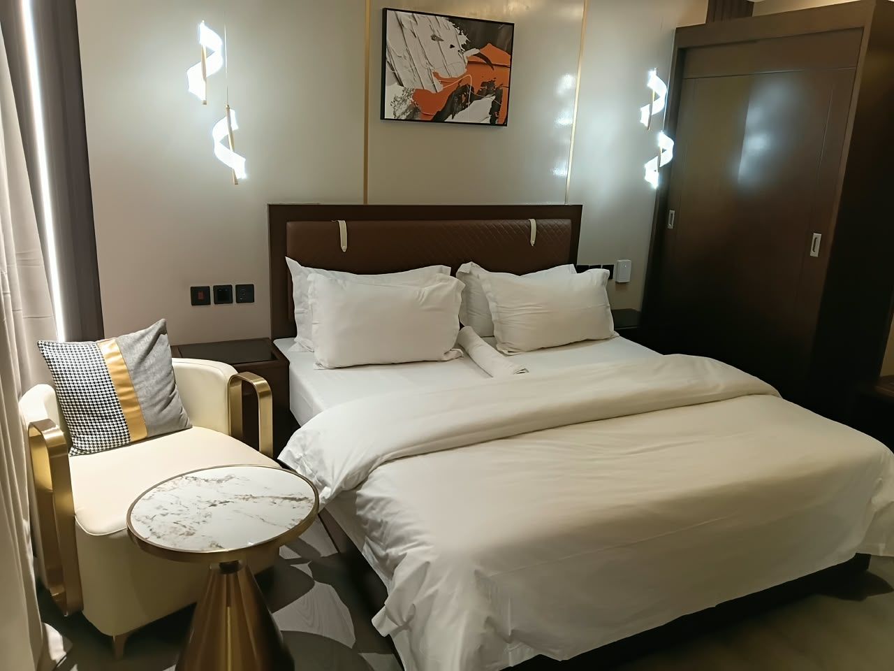 Una camera d'albergo con un letto, un comodino, una sedia e un'opera d'arte appesa al muro.