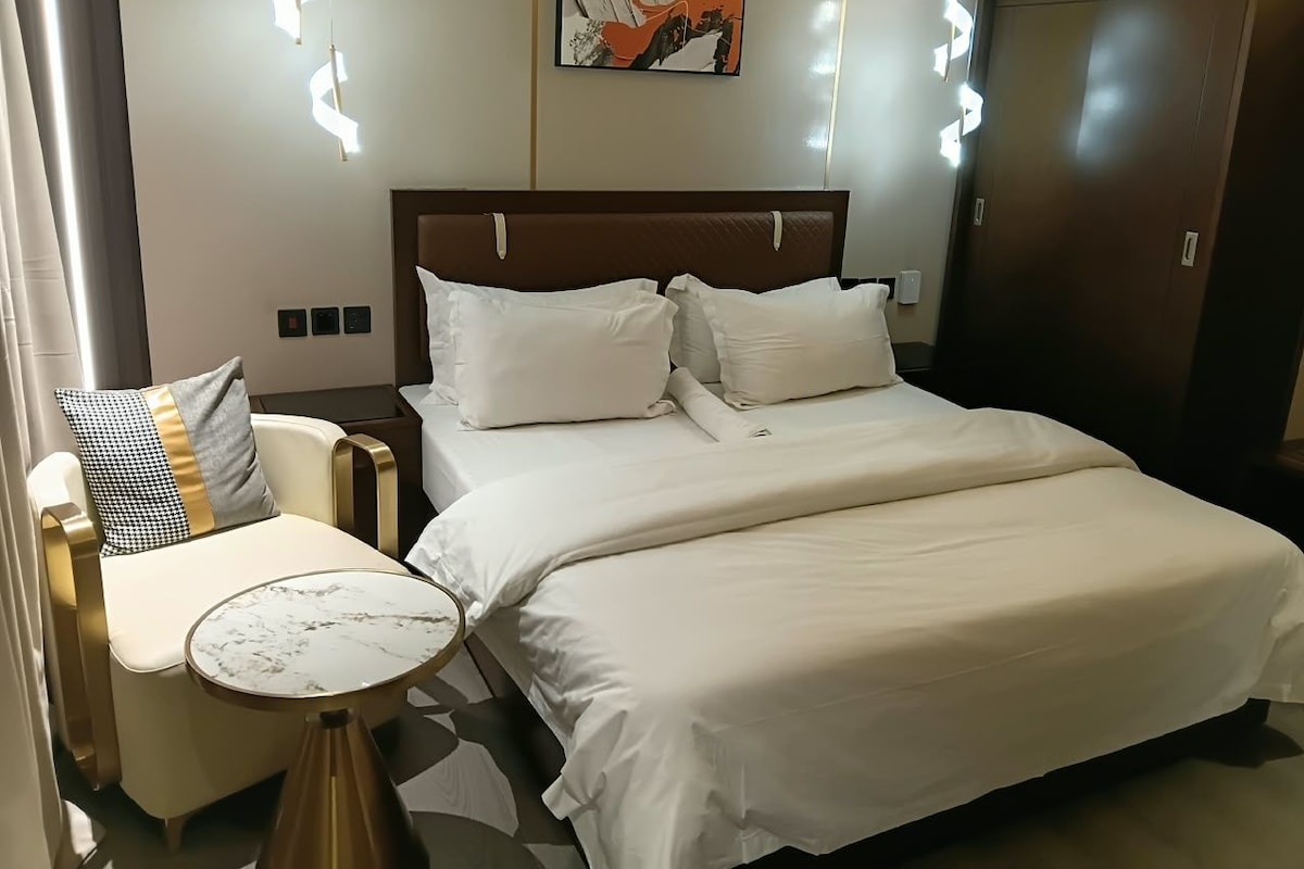 Ein Hotelzimmer mit Bett, Nachttisch, Stuhl und einem Kunstwerk an der Wand.