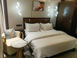 Una habitación de hotel con cama, mesita de noche, silla y una obra de arte en la pared.