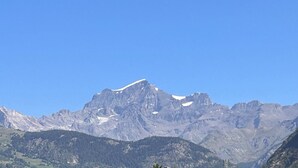 Ein Gebirge mit einem markanten Gipfel, bewaldeten Tälern und blauem Himmel.