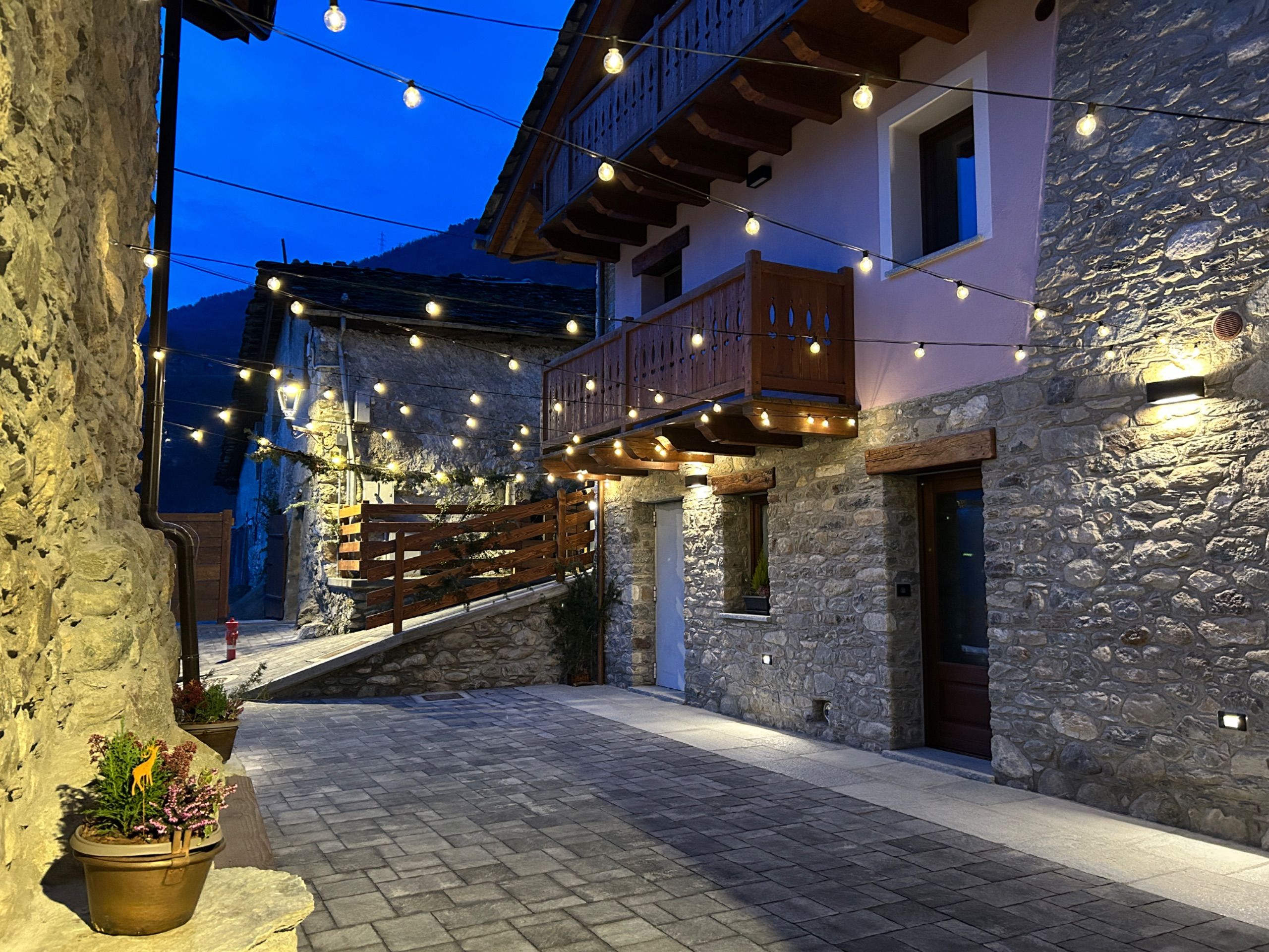 A stone building with a wooden balcony, string lights, and a paved courtyard.
