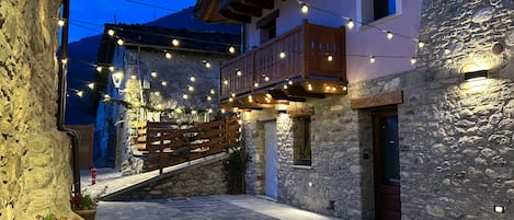 A stone building with a wooden balcony, string lights, and a paved courtyard.