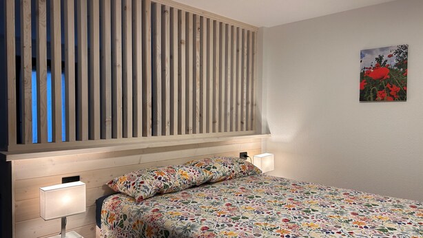 Ein Schlafzimmer mit einem Lattenrost-Kopfteil, einer blumigen Bettdecke und einem Bild an der Wand.