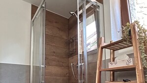 Eine Dusche mit Glastüren, Holzvertäfelung und einem Holzregal mit Korb.
