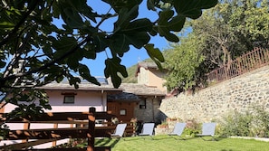 A stone house with a sloped roof, a wooden fence, and a grassy lawn with lounge chairs.