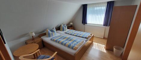 Ein Hotelzimmer mit zwei Betten, einem Schreibtisch, einem Stuhl, einer Heizung und einem Vorhangfenster.