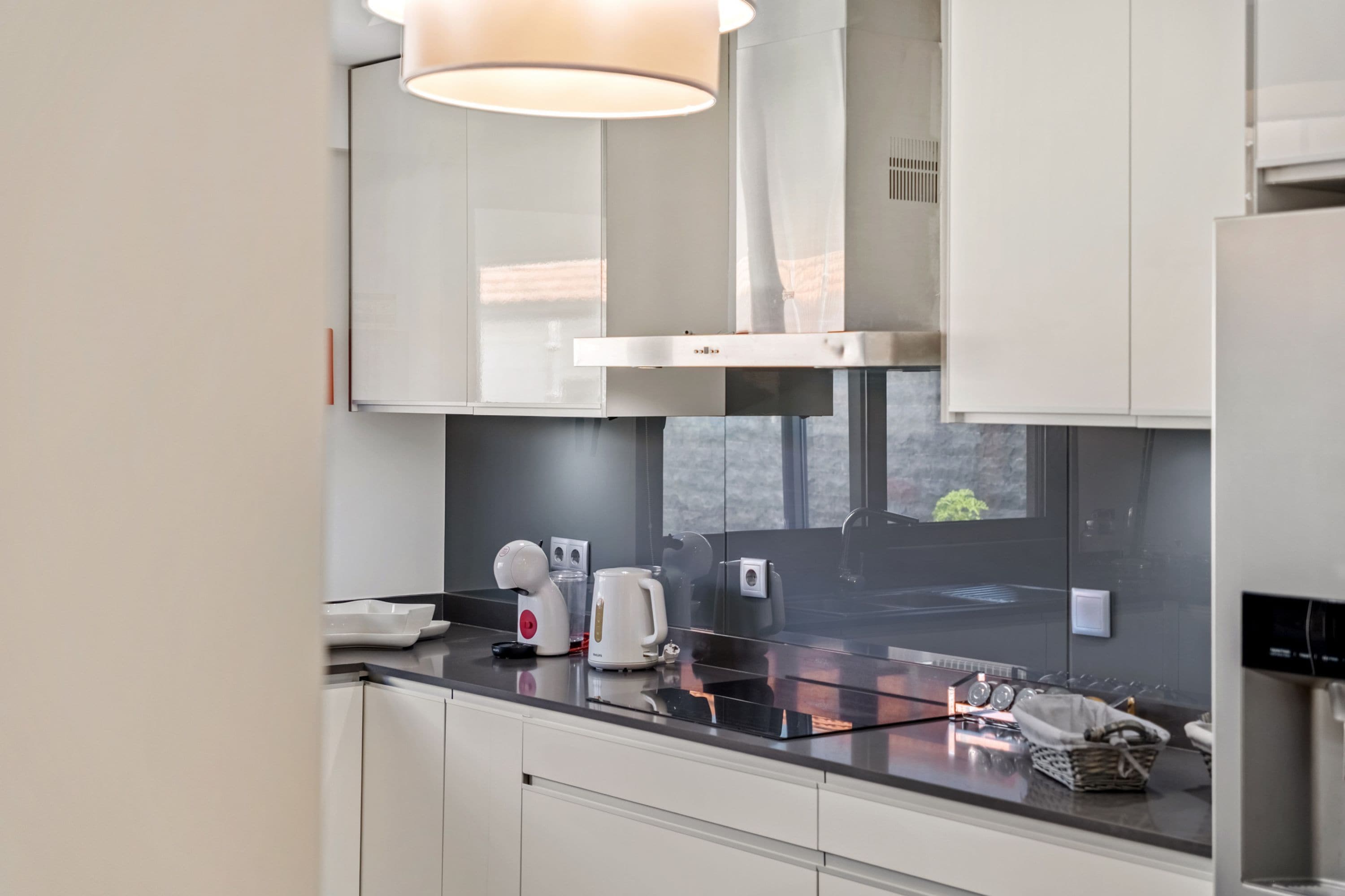 Una cocina moderna con encimera negra, armarios blancos y una campana extractora de acero inoxidable.
