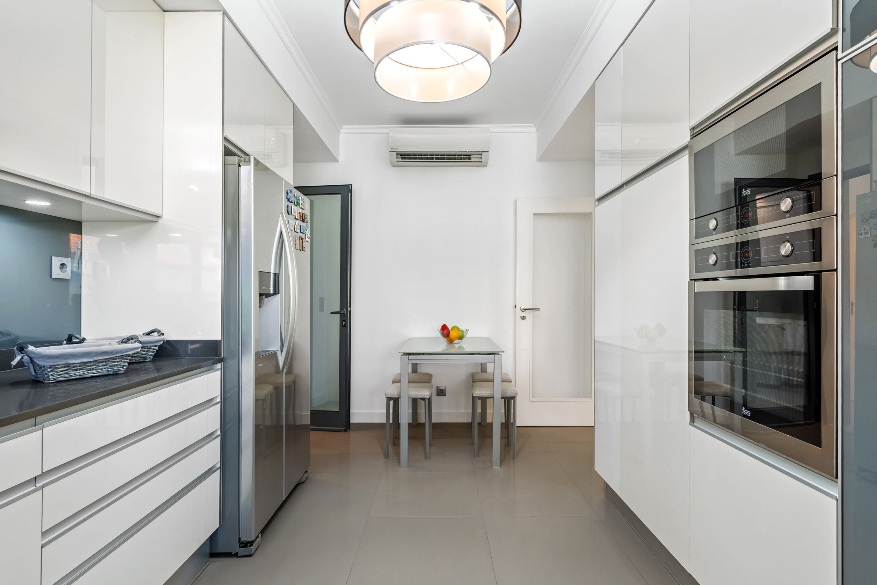 A modern kitchen with white cabinetry, a built-in oven, and a dining area with a table and chairs.