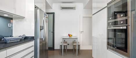 A modern kitchen with white cabinetry, a built-in oven, and a dining area with a table and chairs.