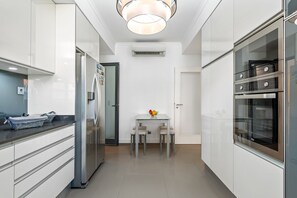 A modern kitchen with white cabinetry, a built-in oven, and a dining area with a table and chairs. - Villa Polaris by Homie (Funchal)