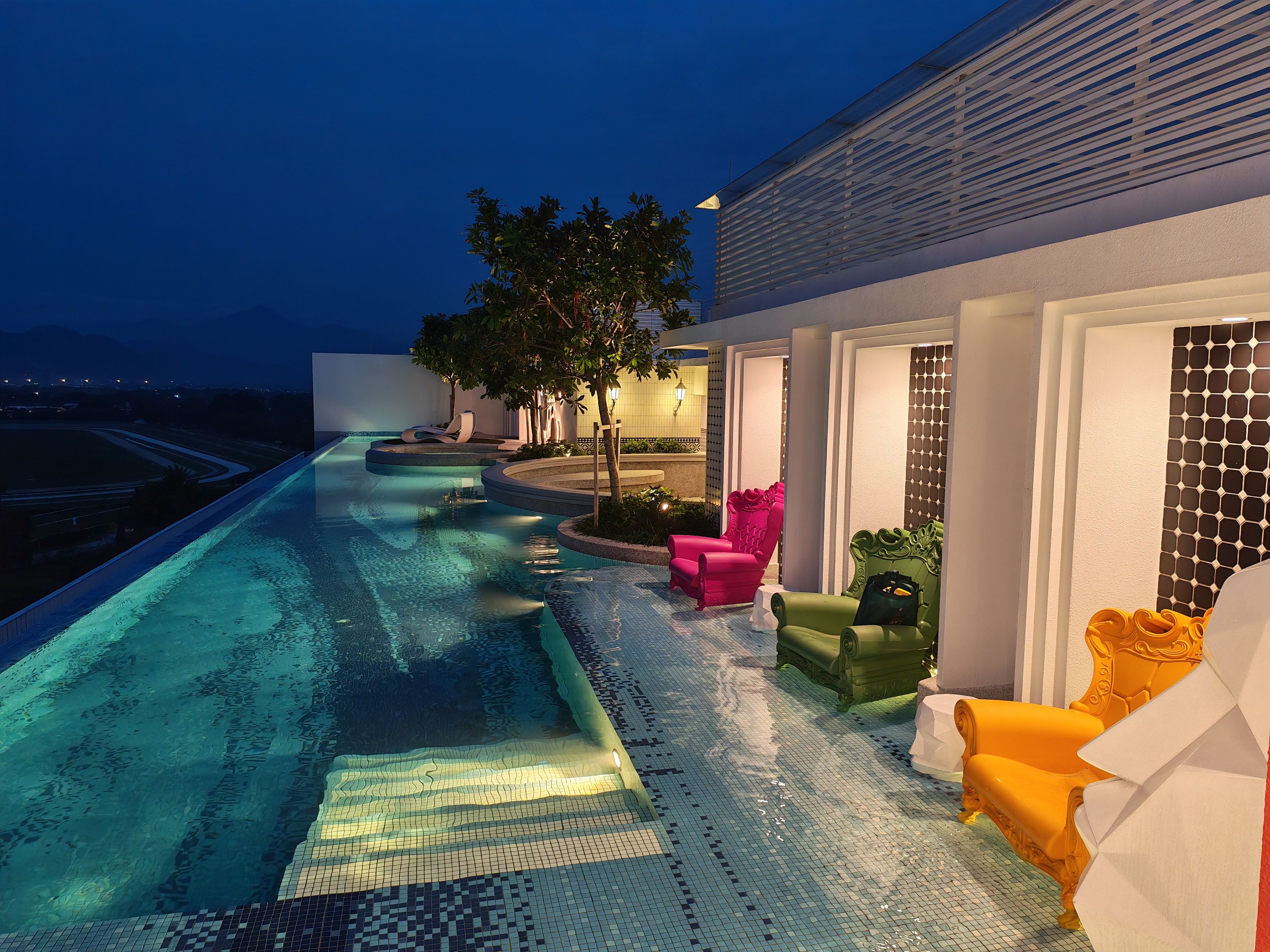 A swimming pool with a tiled edge, surrounded by outdoor seating with cushions.