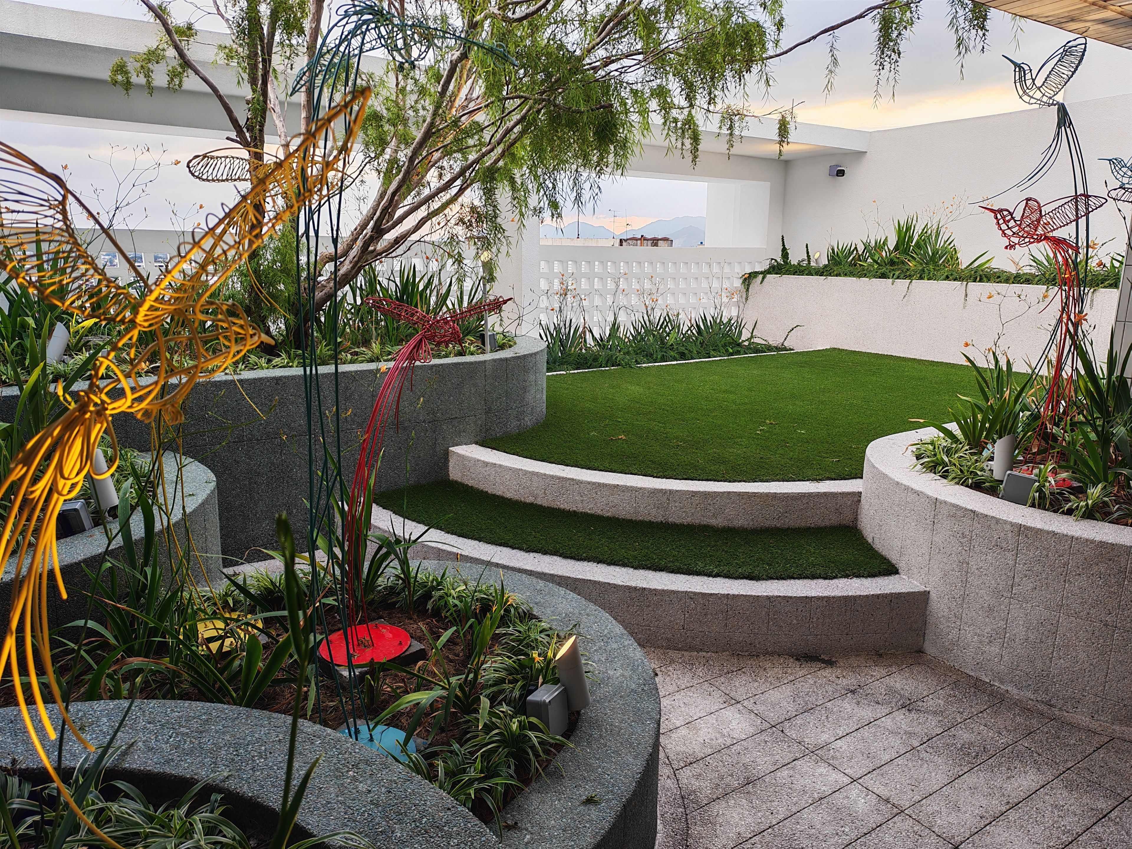 A landscaped garden with a lawn, curved stone planters, and decorative metal sculptures.