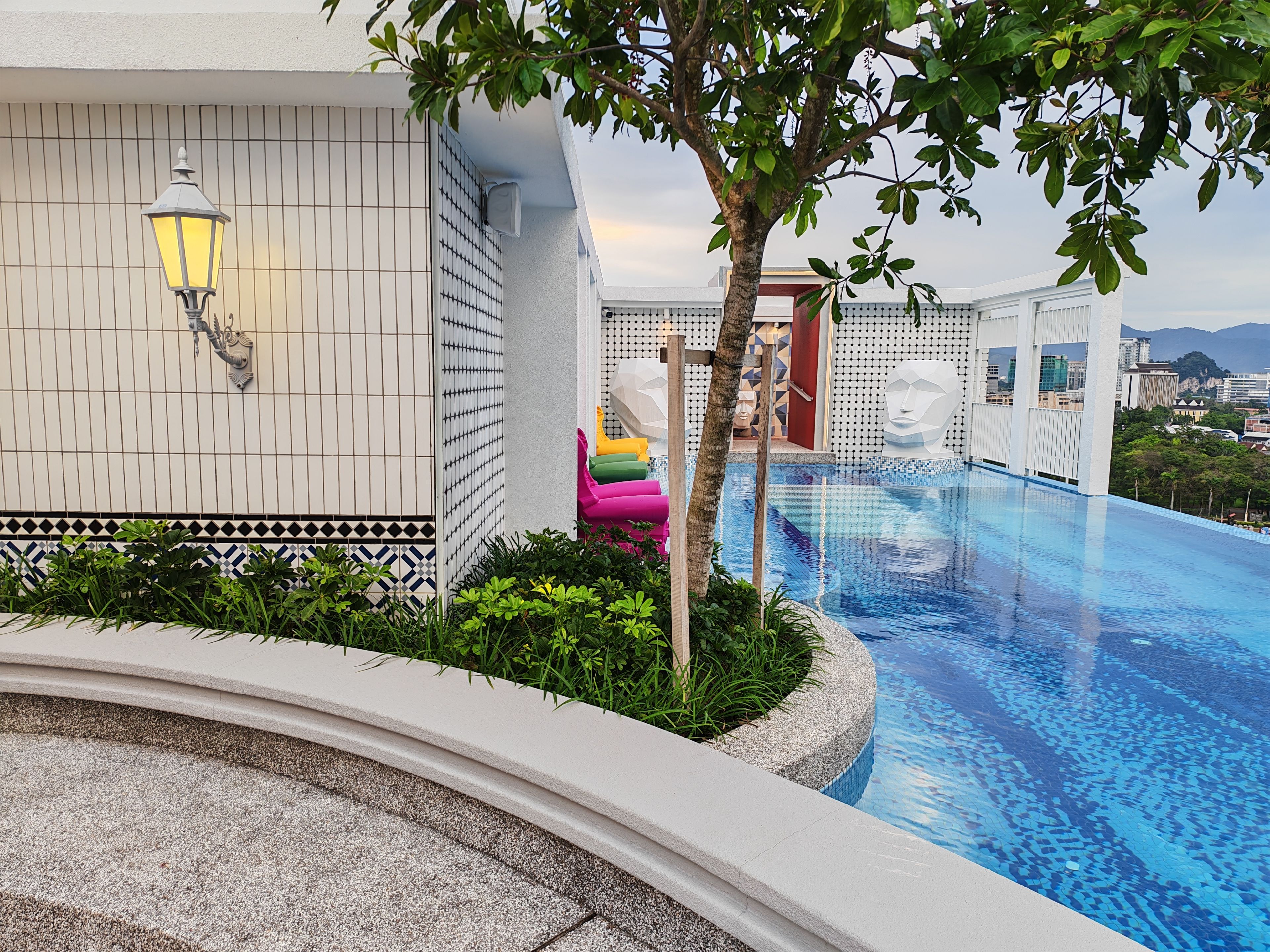 A swimming pool with a tiled edge, a lamp post, and a tree.