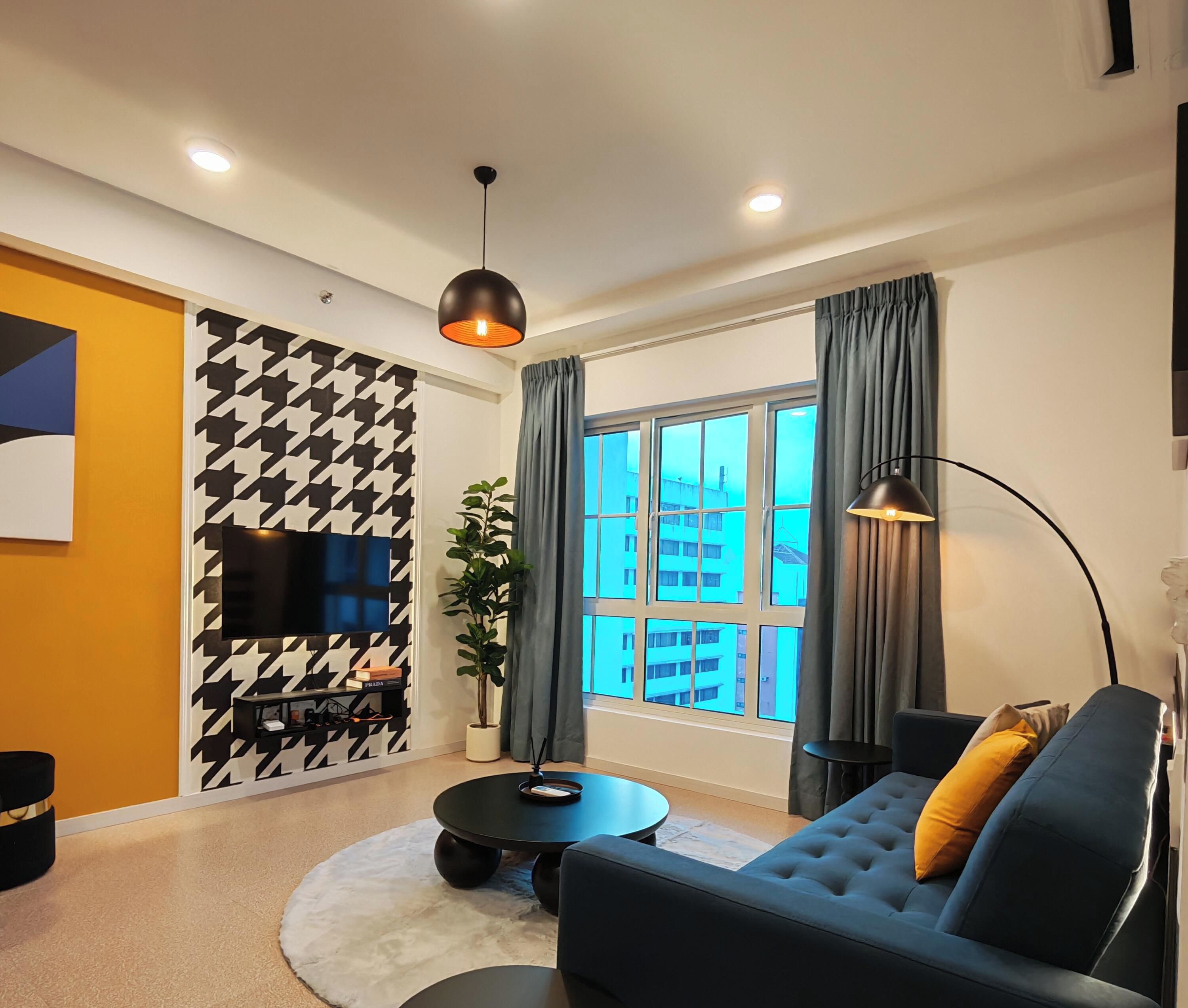 A modern living room with a sofa, a coffee table, a TV, and a large window with curtains.