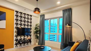 A modern living room with a sofa, a coffee table, a TV, and a large window with curtains.