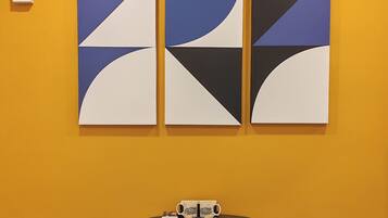 A room with a yellow wall, a round table with a tray of mugs, and three abstract paintings.