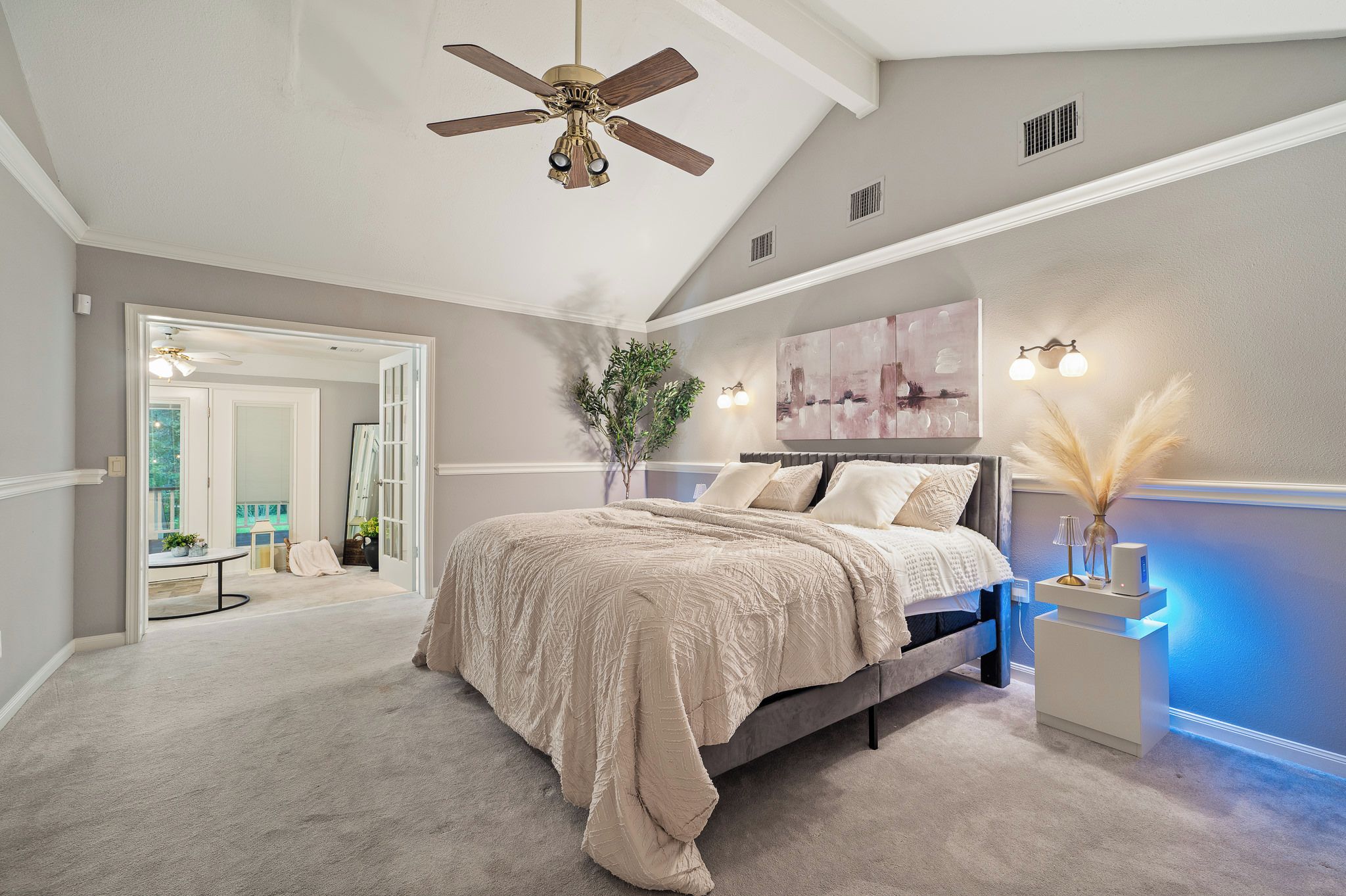 A bedroom with a bed, ceiling fan, artwork, bedside lamp, and a nightstand.