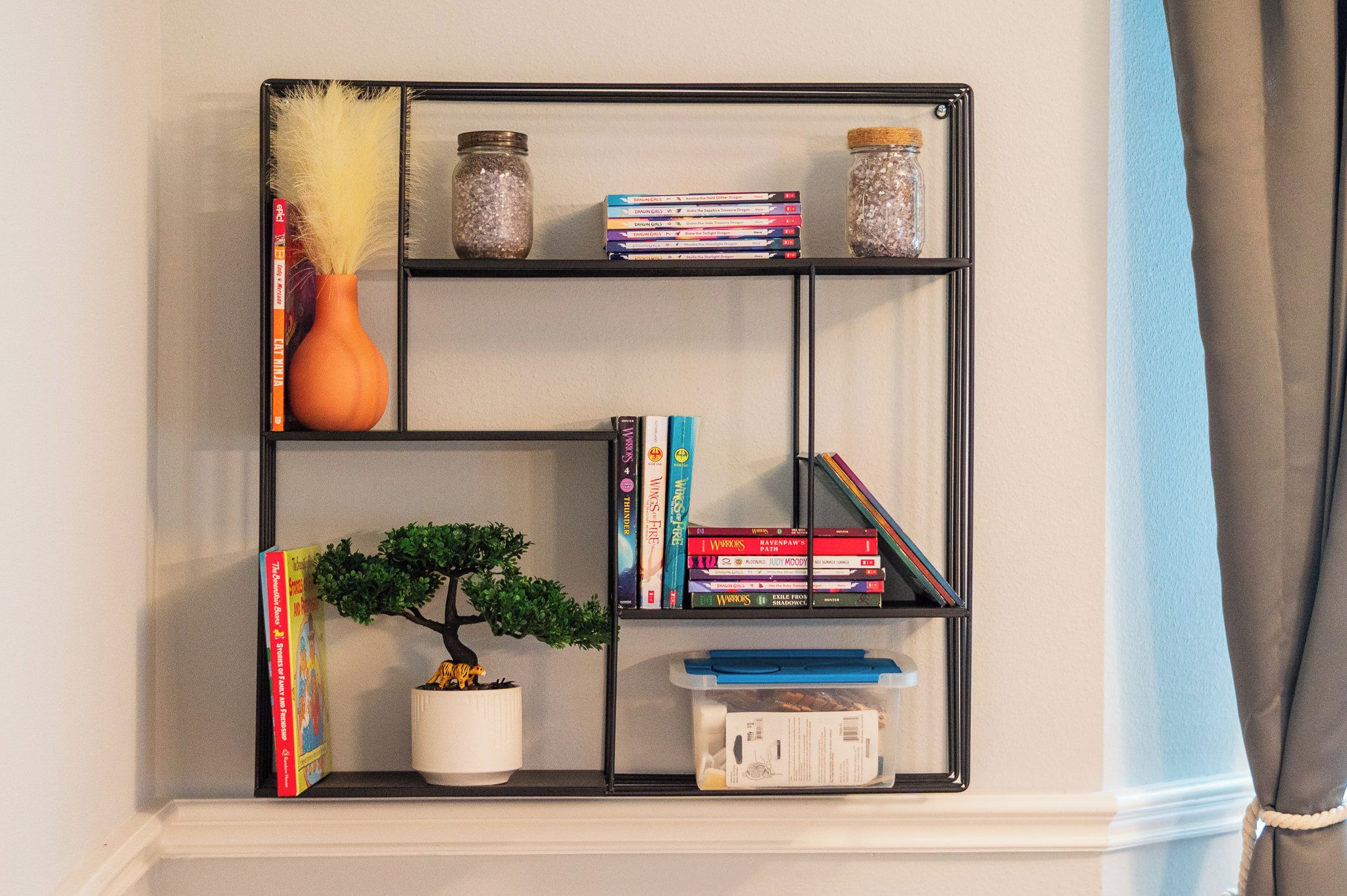 A black metal shelf with books, a small potted plant, decorative jars, and a feather duster.