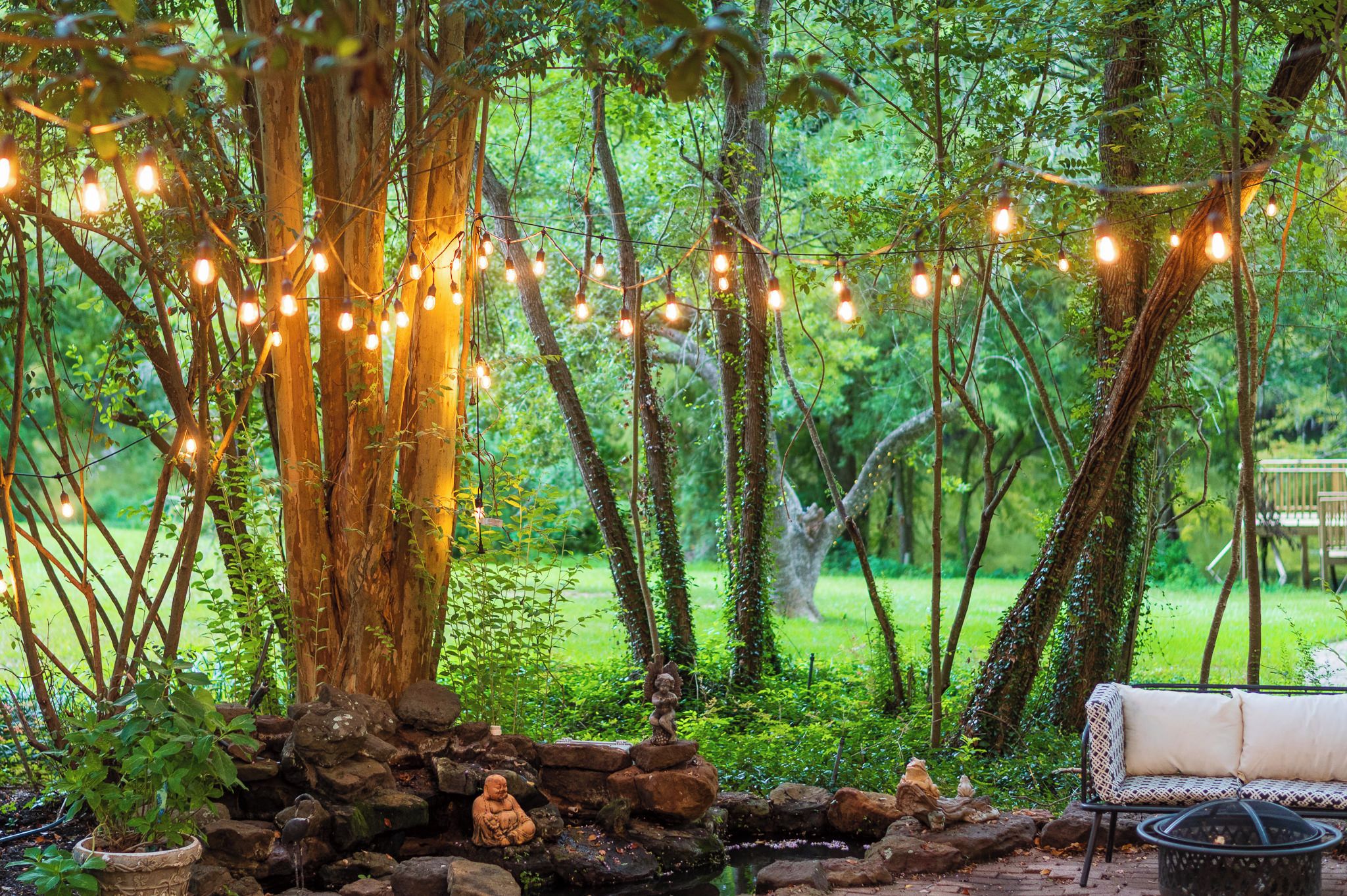 A garden with a stone bench, a tree, and string lights.