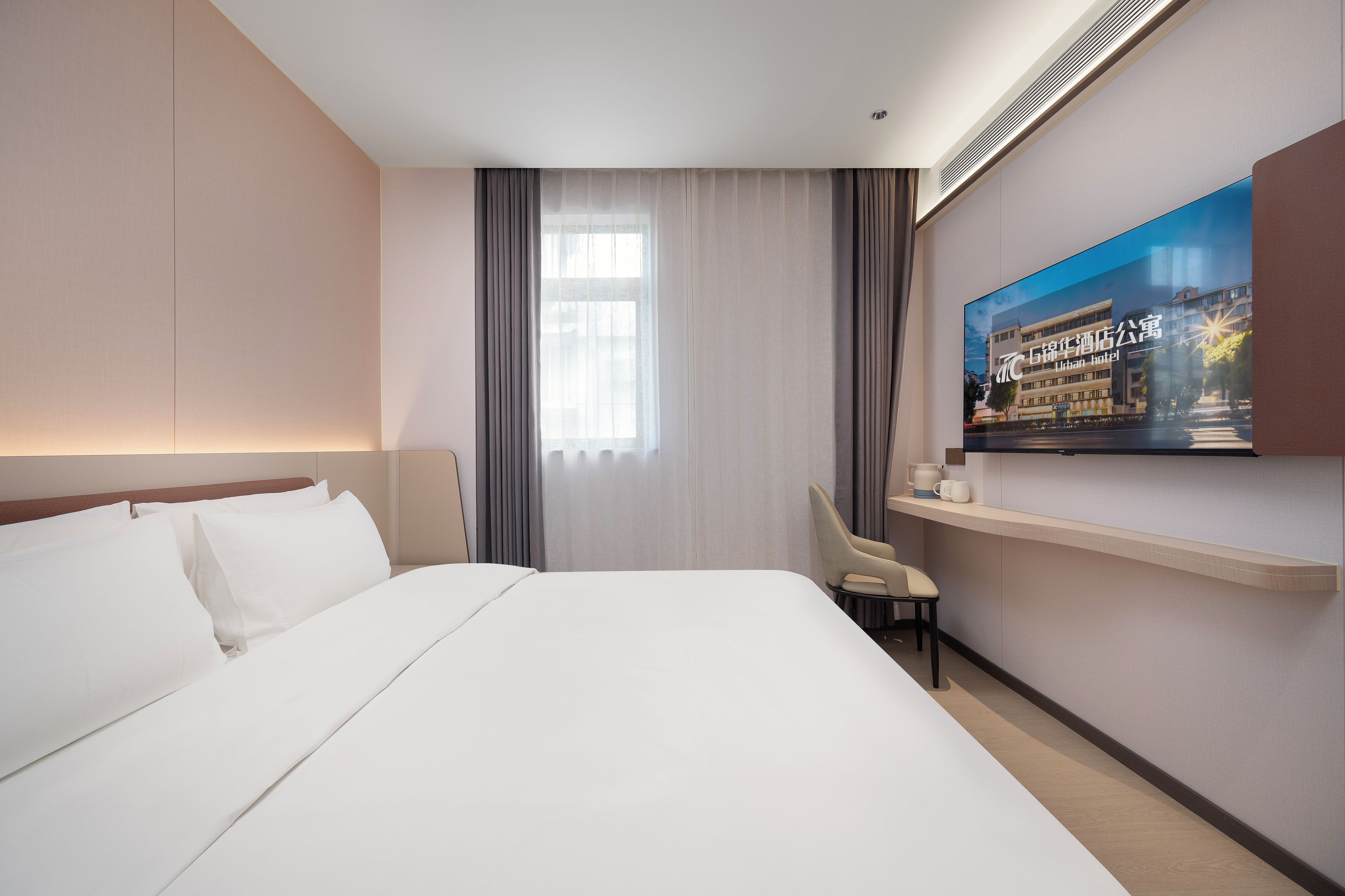 A hotel room with a large bed, a television mounted on the wall, and a window with curtains.