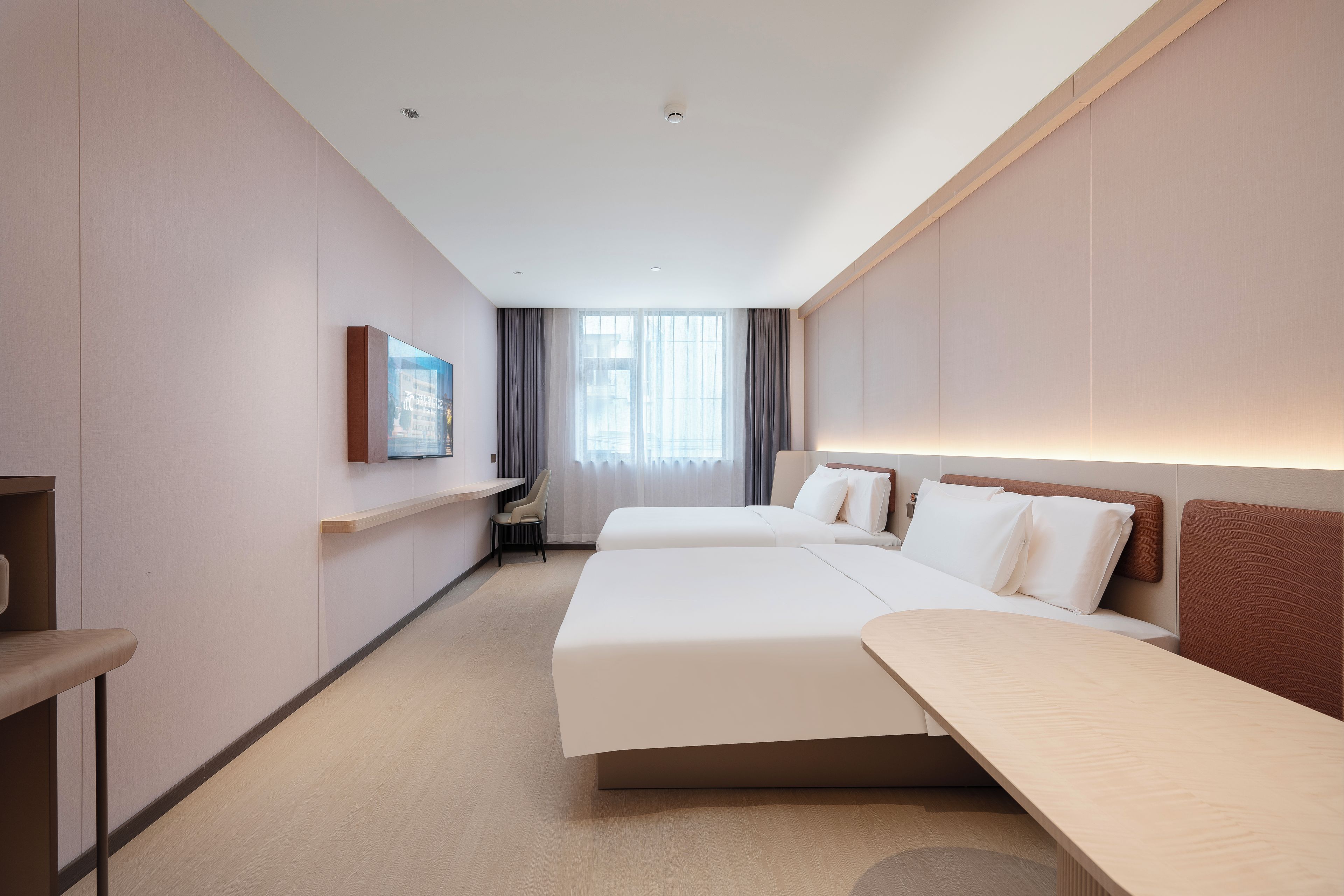 A hotel room with two beds, a desk, a chair, and a window with curtains.