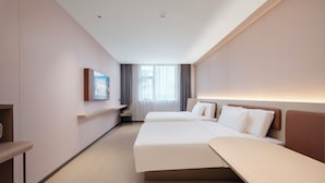 Une chambre d’hôtel avec deux lits, un bureau, une chaise et une fenêtre avec des rideaux.