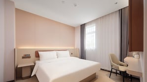 Une chambre d’hôtel avec un lit, un bureau, une chaise, une table de chevet et une fenêtre avec des rideaux.