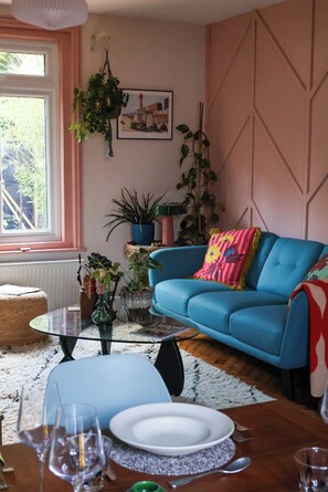 Ein Wohnzimmer mit einem blauen Sofa, einem Glastisch und mehreren Pflanzen.