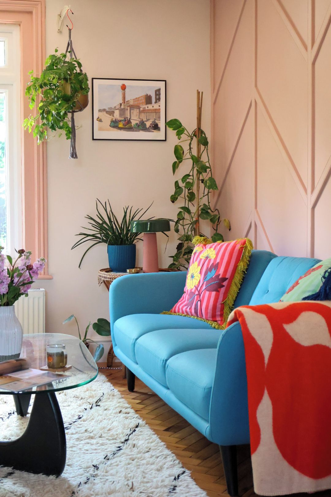 A room with a blue sofa, a glass coffee table, a white furry rug, and various plants.