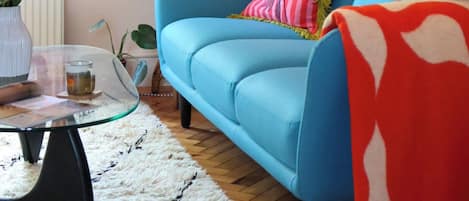 A room with a blue sofa, a glass coffee table, a white furry rug, and various plants.