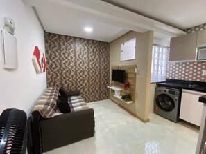 A compact living space with a sofa, a washing machine, a television mounted on a wooden panel, and a patterned wall. - Apartment 101 · 101 Flat Good taste and quality (Belém)