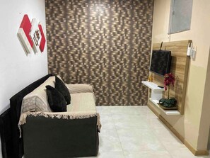 A modern bedroom with a bed, a TV, a decorative wall, and a small shelf with a plant. - Apartment 101 · 101 Flat Good taste and quality (Belém)