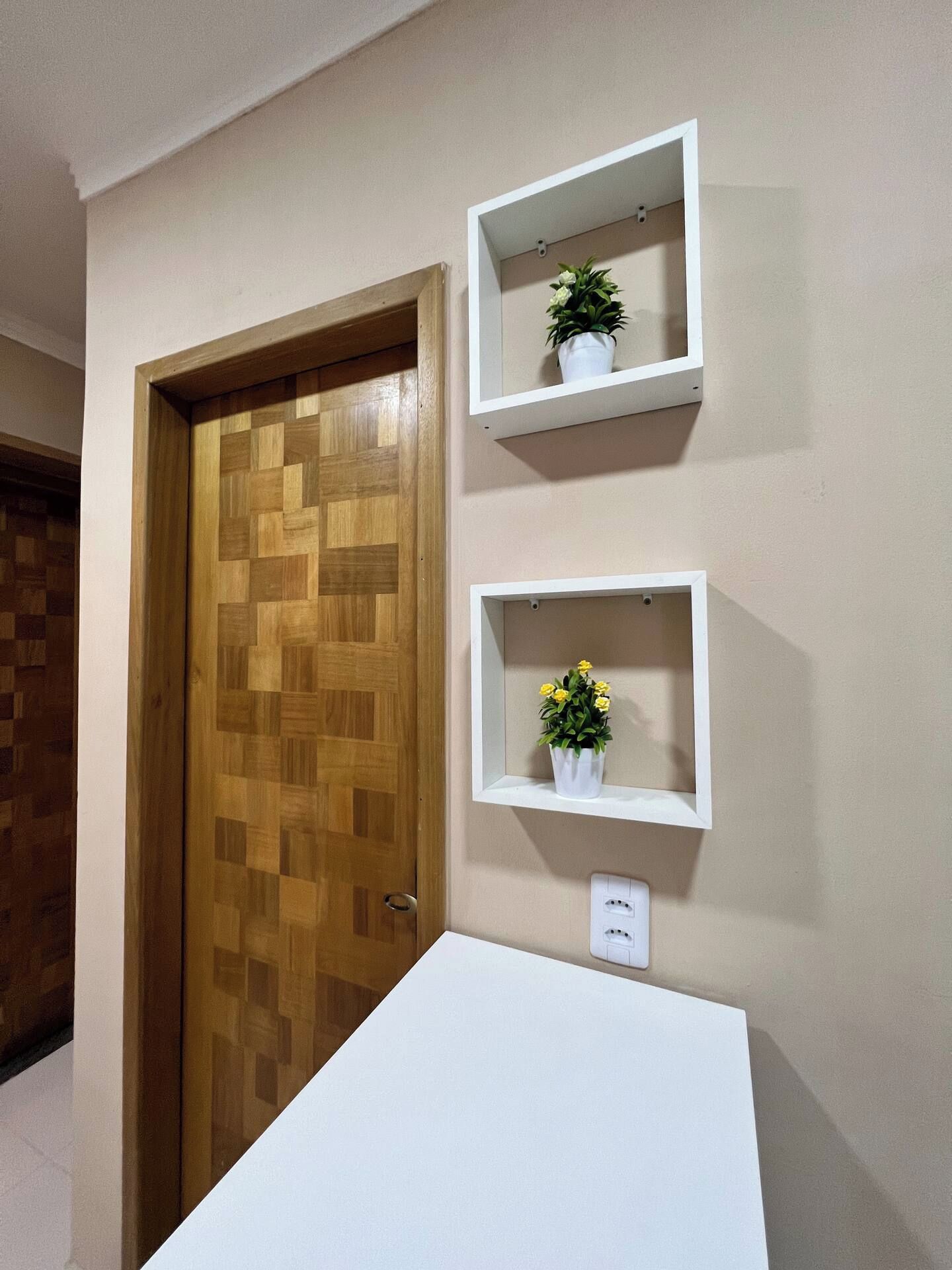 Ein Zimmer mit einer Holztür, zwei weißen Wandregalen und einem weißen Tisch.