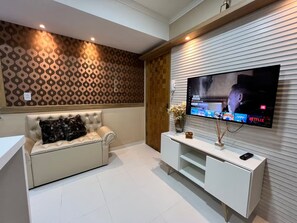 A modern living room with a flat-screen TV mounted on a wall, a white sofa with decorative pillows, and a minimalist white entertainment unit. - 102 Welcoming and cozy (Belém)