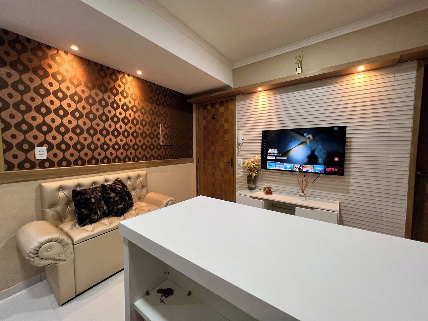 A modern living room with a sofa, a flat-screen TV mounted on a wall, and a white entertainment unit.