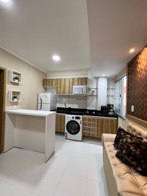 Une cuisine compacte équipée d’un lave-linge, d’un four à micro-ondes et d’un petit plan de travail.