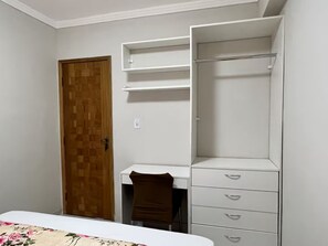 Une chambre à coucher avec un lit, une porte en bois, un bureau et une armoire blanche avec des tiroirs.