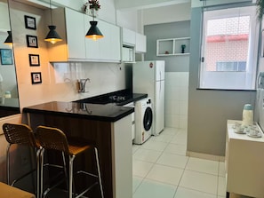 Een kleine keuken met een centraal eiland, een wasmachine en een koelkast.