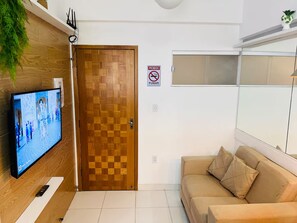 A room with a wooden door, a television on the wall, a sofa, and a sign prohibiting smoking. - 103 Beautiful and Delicate Apartment (Belém)