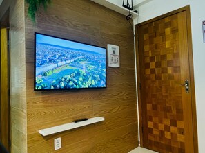 A television mounted on a wooden wall, a door with a checkered pattern, and a white shelf below the TV. - 103 Beautiful and Delicate Apartment (Belém)