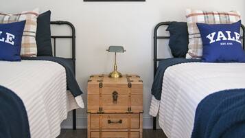 Une chambre avec deux lits, une commode en bois, une lampe et un tableau encadré au mur.