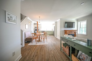 Een ruime keuken met houten vloeren, een eethoek met een ronde tafel en stoelen, en een groene bank met manden.