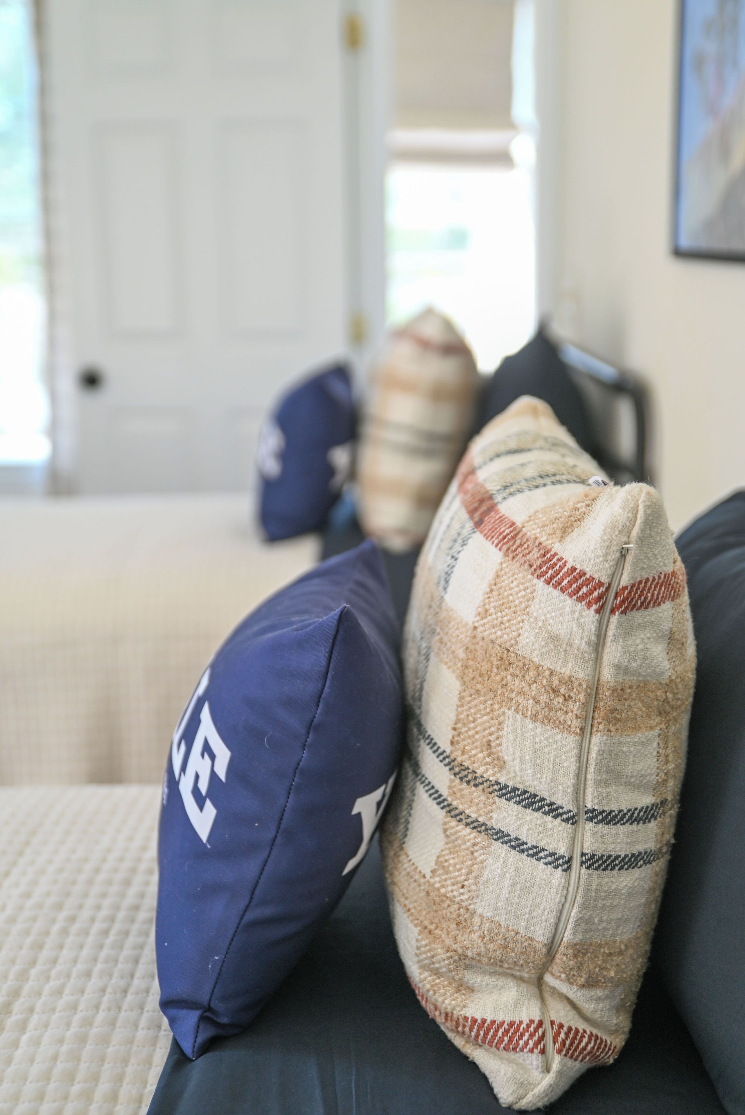 A close-up of a couch with a pillow featuring a checkered pattern and a pillow with a white logo.