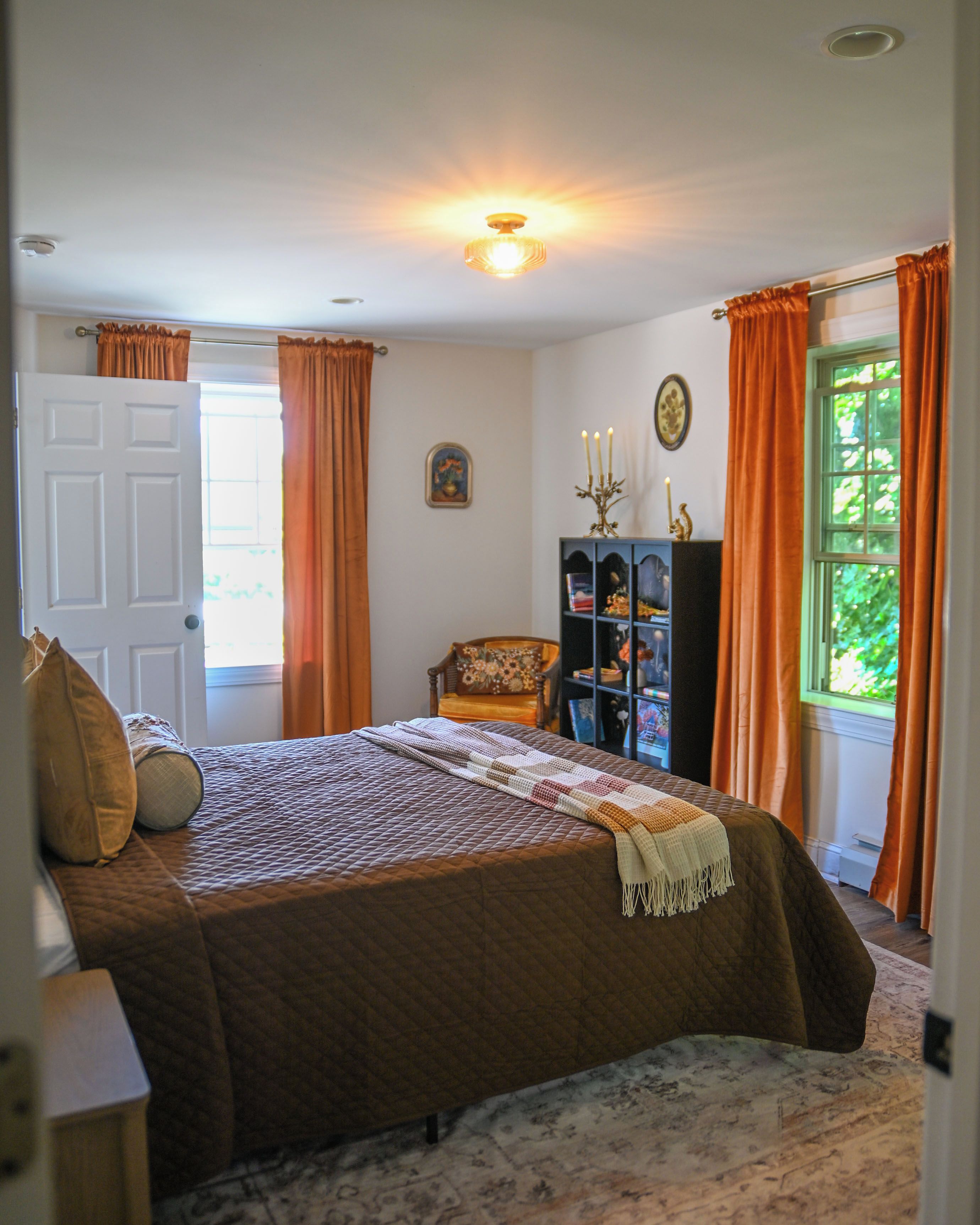 A bedroom with a bed, a chair, a bookshelf, and a window with curtains.