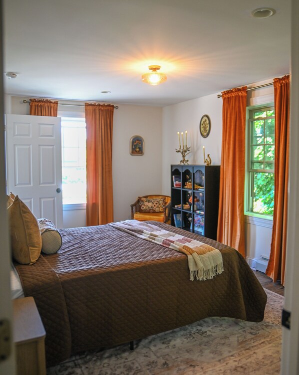 A bedroom with a bed, a chair, a bookshelf, and a window with curtains.