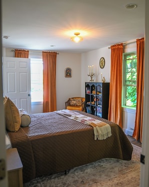 A bedroom with a bed, a chair, a bookshelf, and a window with curtains.