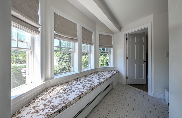 A room with a built-in bench along a wall with large windows, a door, and a tiled floor.