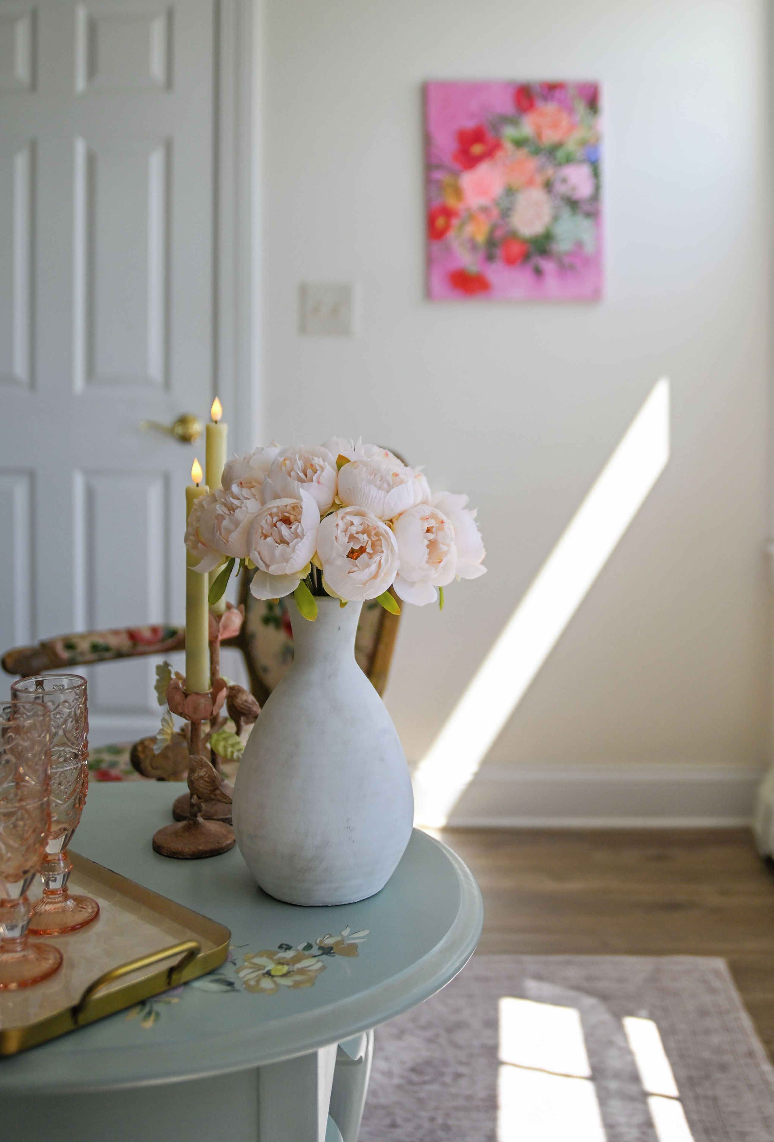 A room with a table featuring a vase of flowers, a candle, and a glass.